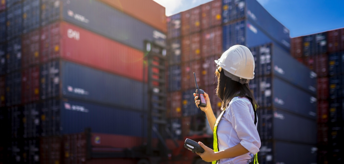 Woman in hard hat in front of stacks of shipping containers