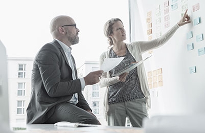 Man and woman organizing post-it notes on a white board.