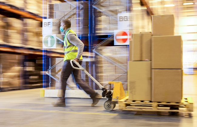 Man with mask pulling hand truck with a pallet of boxes