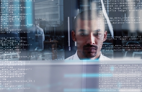 Photo of man sitting at a computer reflected in glass