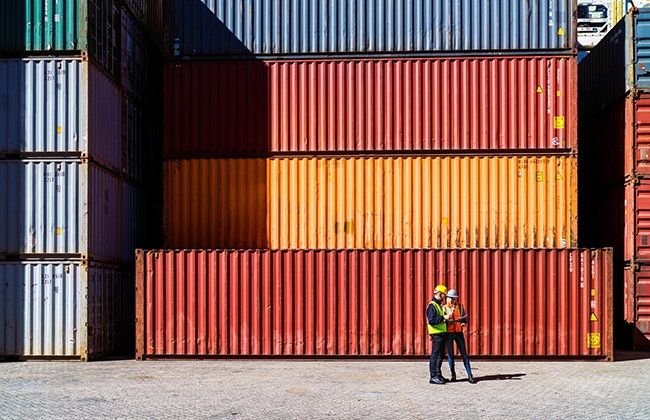 Workers walking in front of a stack of shipping containers