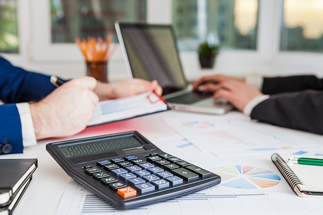 Calculator at a desk with two people working