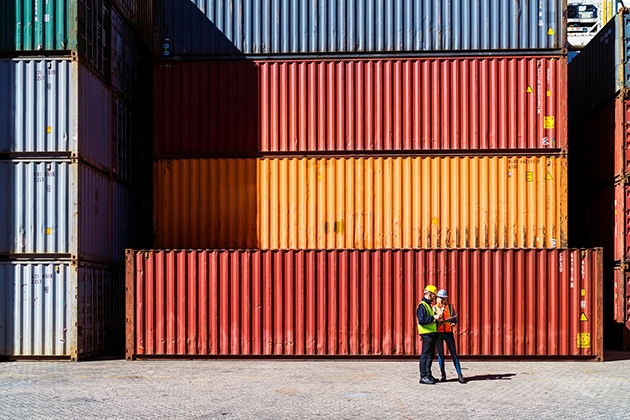 Workers walking in front of a stack of shipping containers